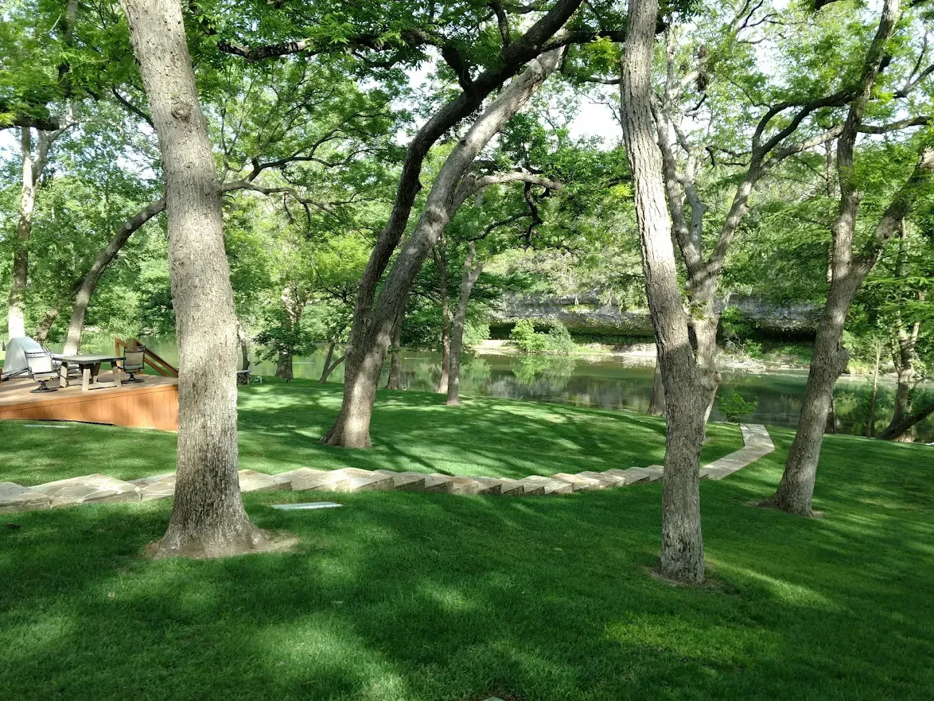 Green lawn with trees in a park-like setting; pathway leads to a body of water.