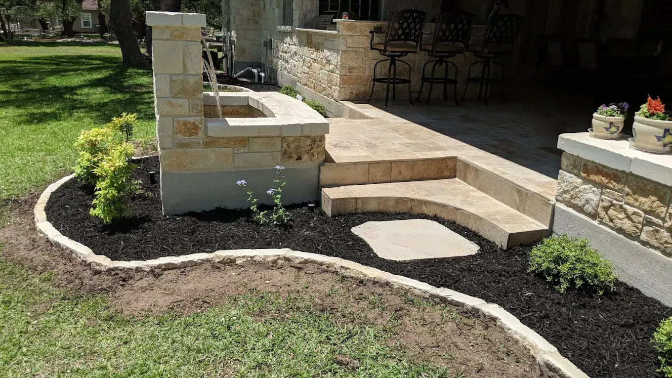 Stone steps and patio with decorative stone accents, black mulch border and greenery.