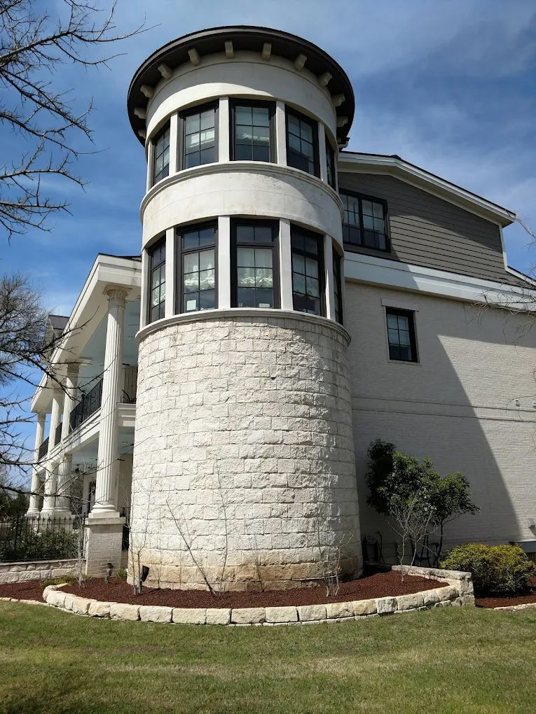White stone tower with black-framed windows and a white top section, attached to a white building with columns.