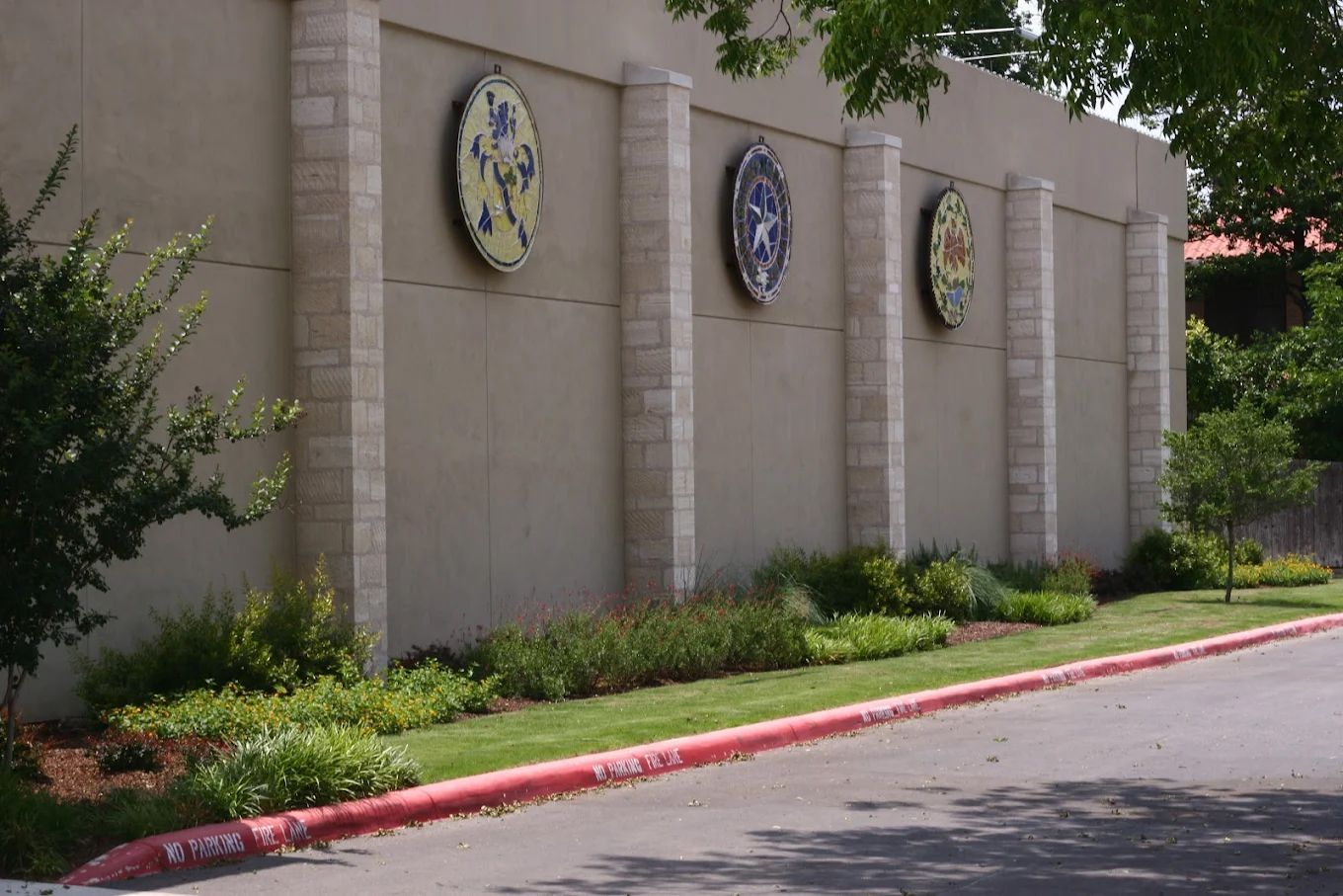 Beige building exterior with three circular emblems, green landscaping, and a red curb.