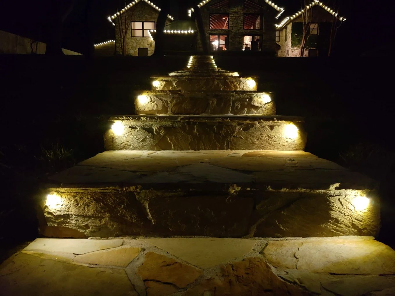 Stone steps illuminated at night, leading up to a house with Christmas lights.