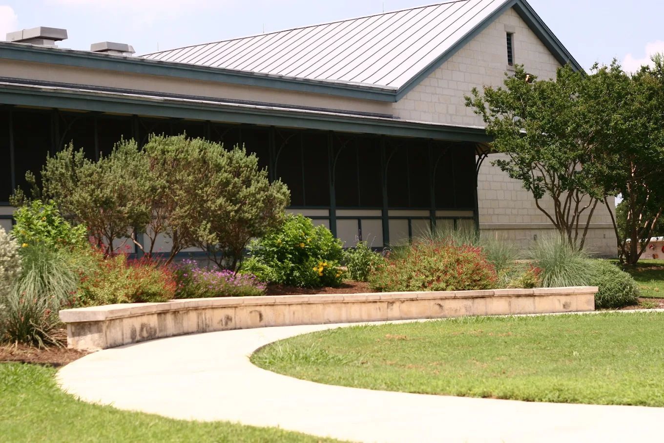 Curved sidewalk leading past a building with a white metal roof and a flower bed.