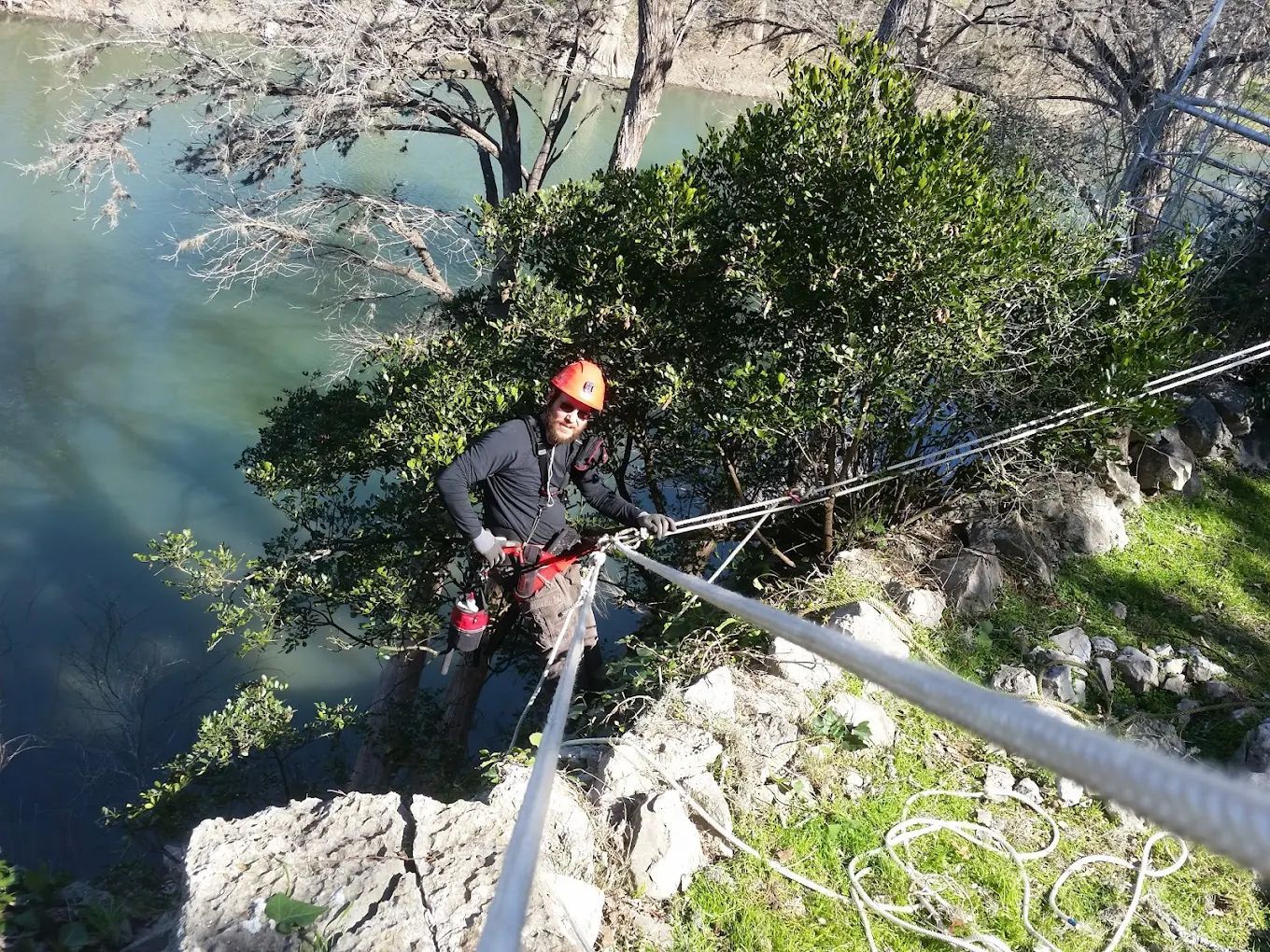 Person in climbing gear rappelling down a cliff face, overlooking a body of water.