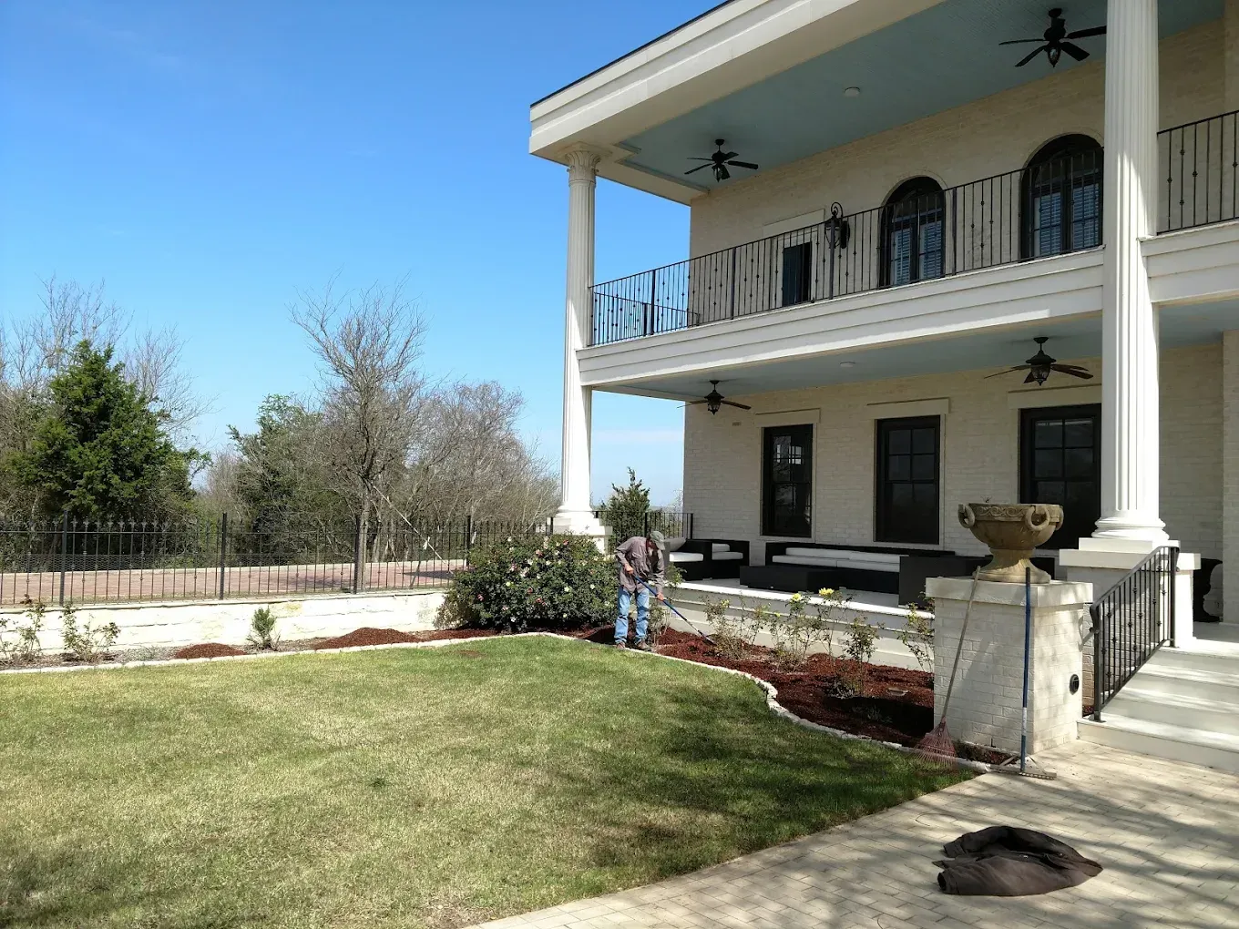 Two-story white house with large columns and a balcony. A person is working in the yard.