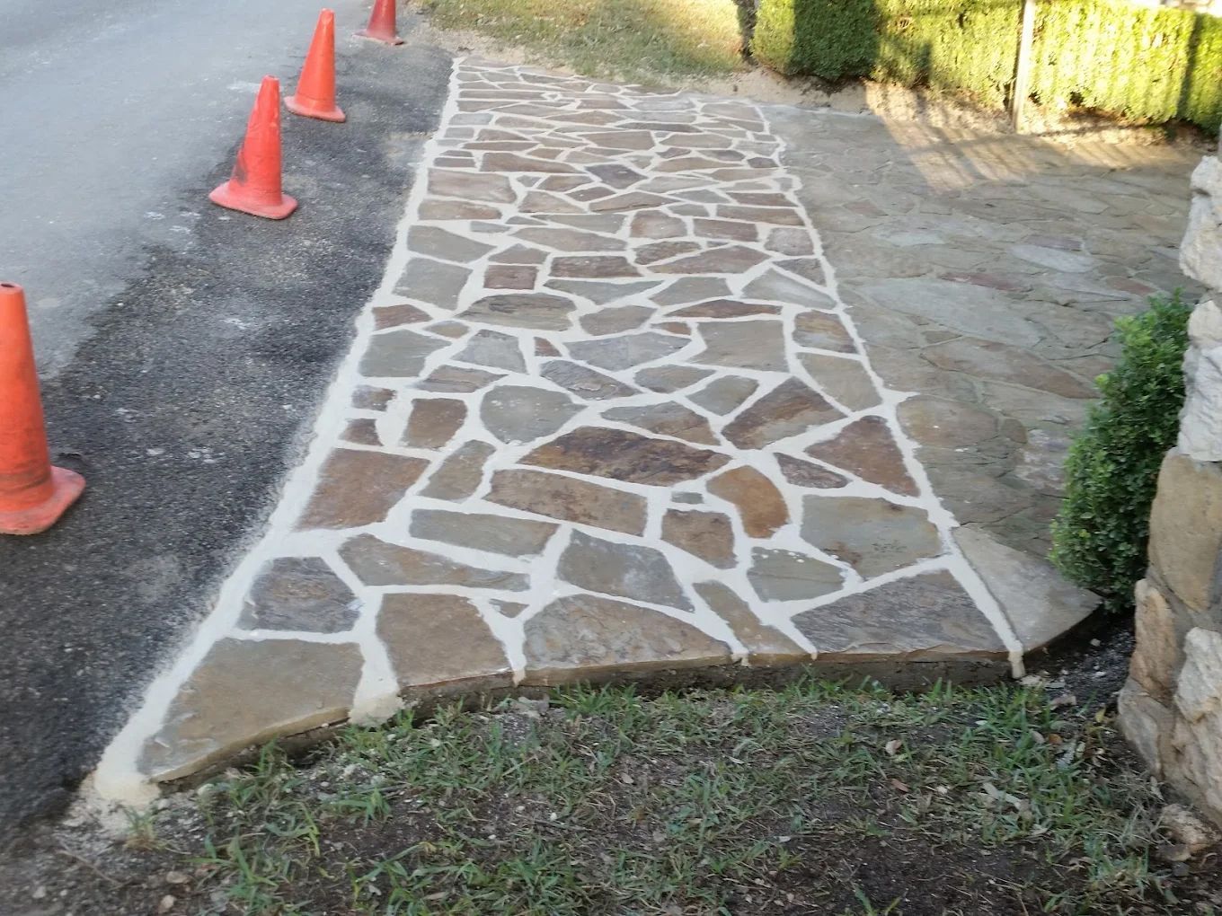 Stone walkway with irregular shaped stones, concrete borders, and orange traffic cones.