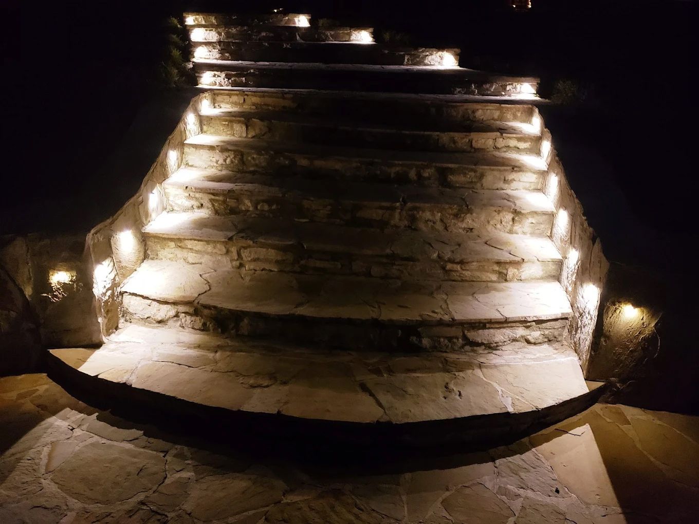 Stone steps illuminated by lights, ascending upwards into darkness.