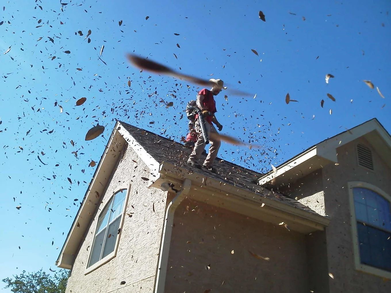 Two people on a rooftop, surrounded by debris. One is holding a large object, blue sky.