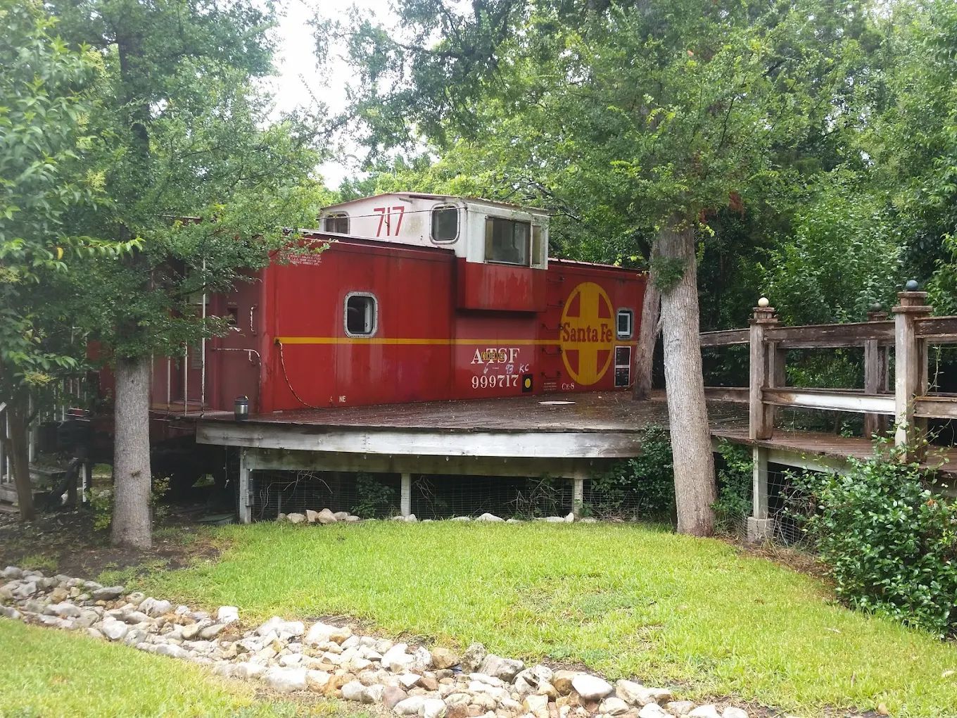 Red Santa Fe caboose on a wooden platform, surrounded by trees and greenery.