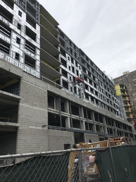 Construction site; multistory building frame with exposed metal studs and concrete block base; cloudy sky.