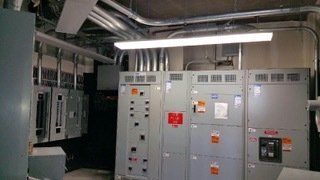 Electrical control panels in a utility room. Gray metal cabinets, conduit, and overhead lighting.