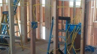 Interior view of a wooden framed wall with electrical wiring and blue junction boxes.