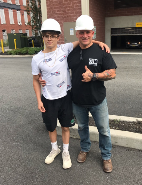 Two people in hard hats stand next to each other in a parking lot. One gives a thumbs up.