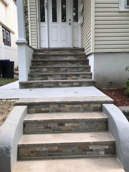 Stone steps leading up to a white door, with a concrete landing and siding house.