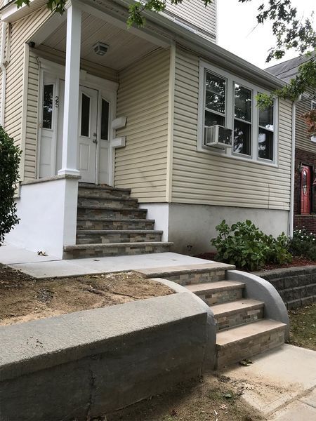 Beige house with porch, steps, and concrete retaining walls.