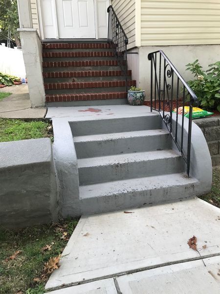 Concrete steps leading to a house with a black metal railing.