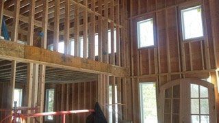 Interior of a house under construction. Wooden framework, windows, and a doorway are visible.