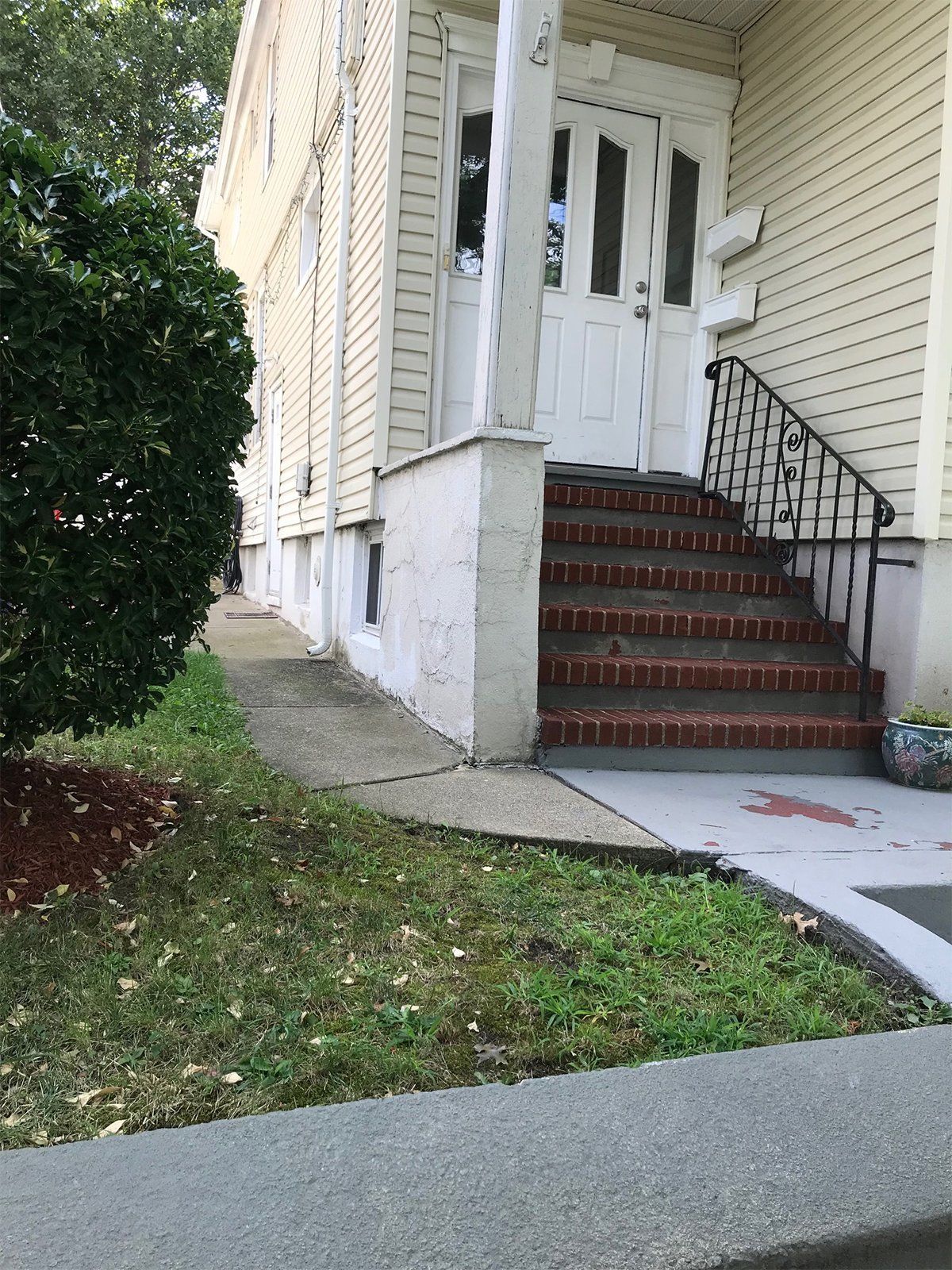 Building entrance with steps, brick stairs, white door, and a black railing.