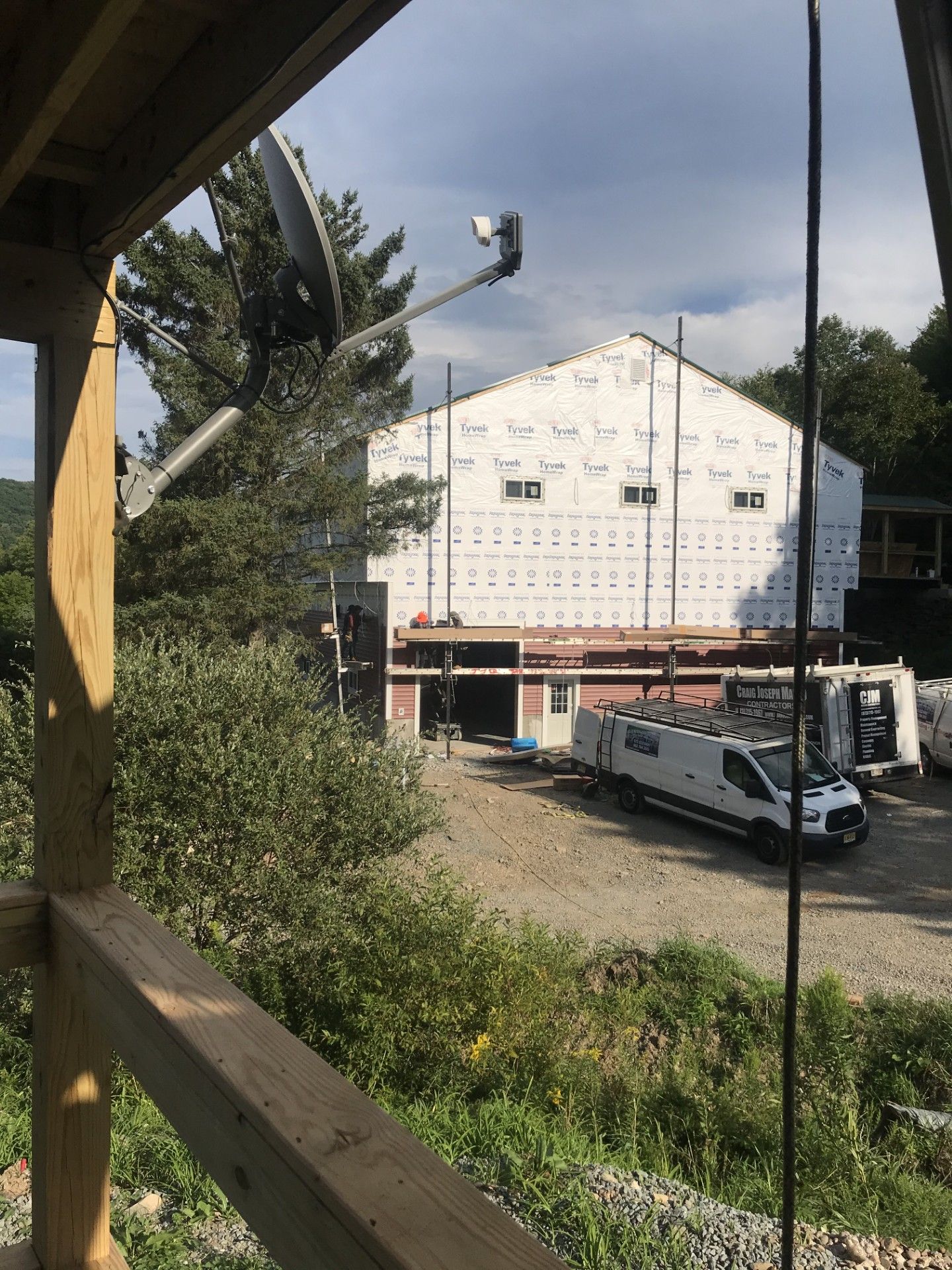 A view from a wooden porch looking out at a large building under construction with a white work van parked nearby.