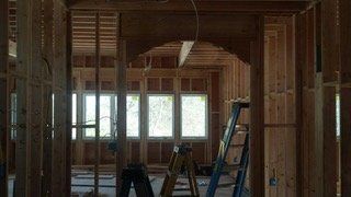 Interior view of a building under construction, framed with wooden studs, featuring an arched doorway and windows.