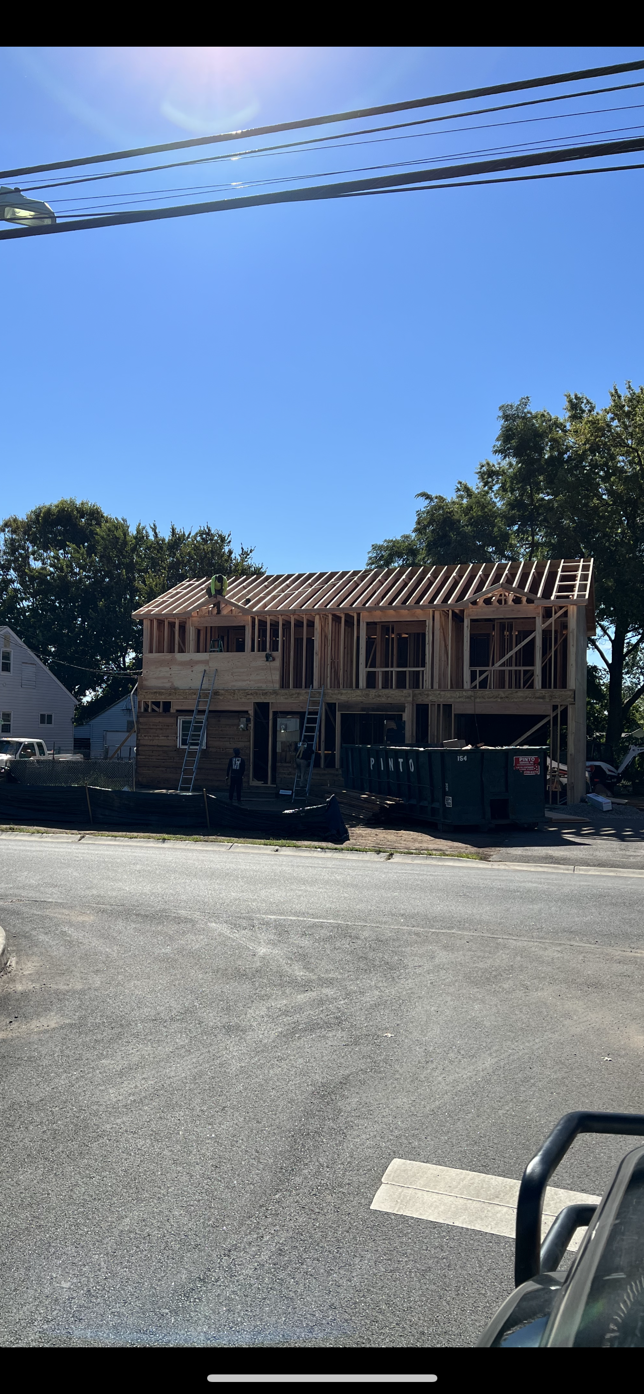 A two-story residential building under construction with exposed wooden framing against a clear blue sky.