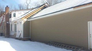 House exterior with partial siding and exposed framing; snow on the ground and roof.