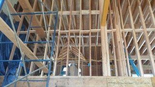 Wooden framing of a building under construction, with scaffolding and wiring visible.