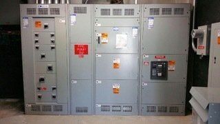Gray electrical panel with various compartments and labels, indoors.