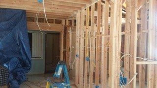 Interior framing of a house under construction with exposed electrical wiring and a blue tarp.