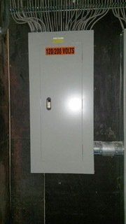 Electrical panel on a wall, labeled 120/208 volts, with conduit and wiring above it.