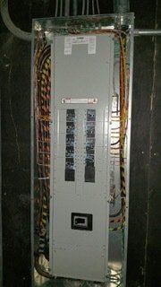 Electrical circuit breaker panel with wires in a metal enclosure. Gray panel with rows of black circuit breakers.