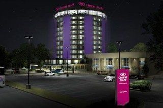 Night view of a purple illuminated Crown Plaza hotel, with a lit sign and parked cars in the lot.