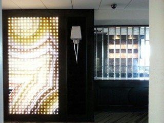Lit display panel beside dark doorway, wall sconce, and mirrored entry.