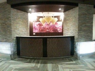 Reception desk with stone walls, decorative panels, and abstract art under a chandelier.