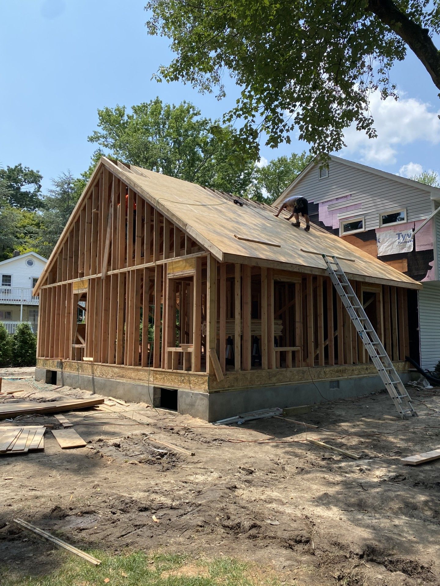 A person works on the wooden roof framing of a new house construction project on a sunny day.