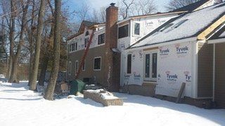 House exterior under construction, covered with Tyvek. Chimney, snow on ground, ladder leaned against wall.