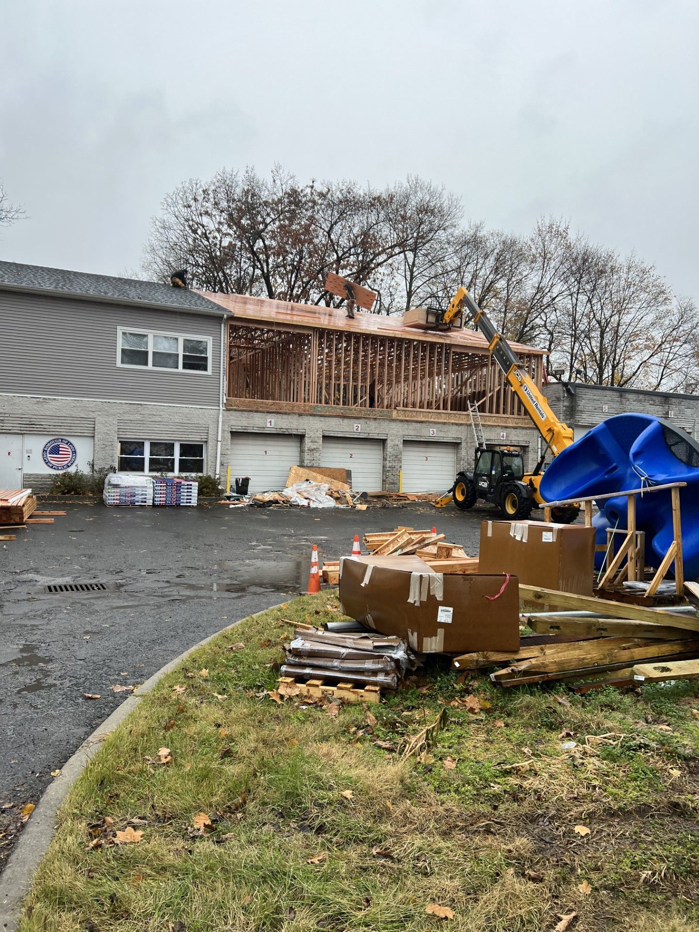 A construction site with a building under renovation, featuring a yellow telehandler and a large blue slide.