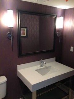 Bathroom with purple walls, white countertop sink, large mirror, and sconce lighting.