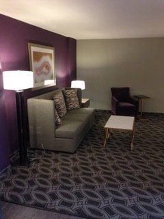 Living room with purple accent wall, sofa, armchair, patterned carpet, and lamps.