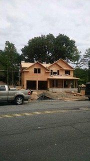 Construction of a two-story house with a garage and porch; a truck is parked in front of the house on a street.