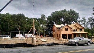 Construction site: partially built house, truck parked in front, trees in background, cloudy sky.