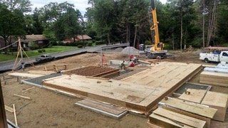 Construction site with a partially built wooden foundation, crane in the background, workers present.