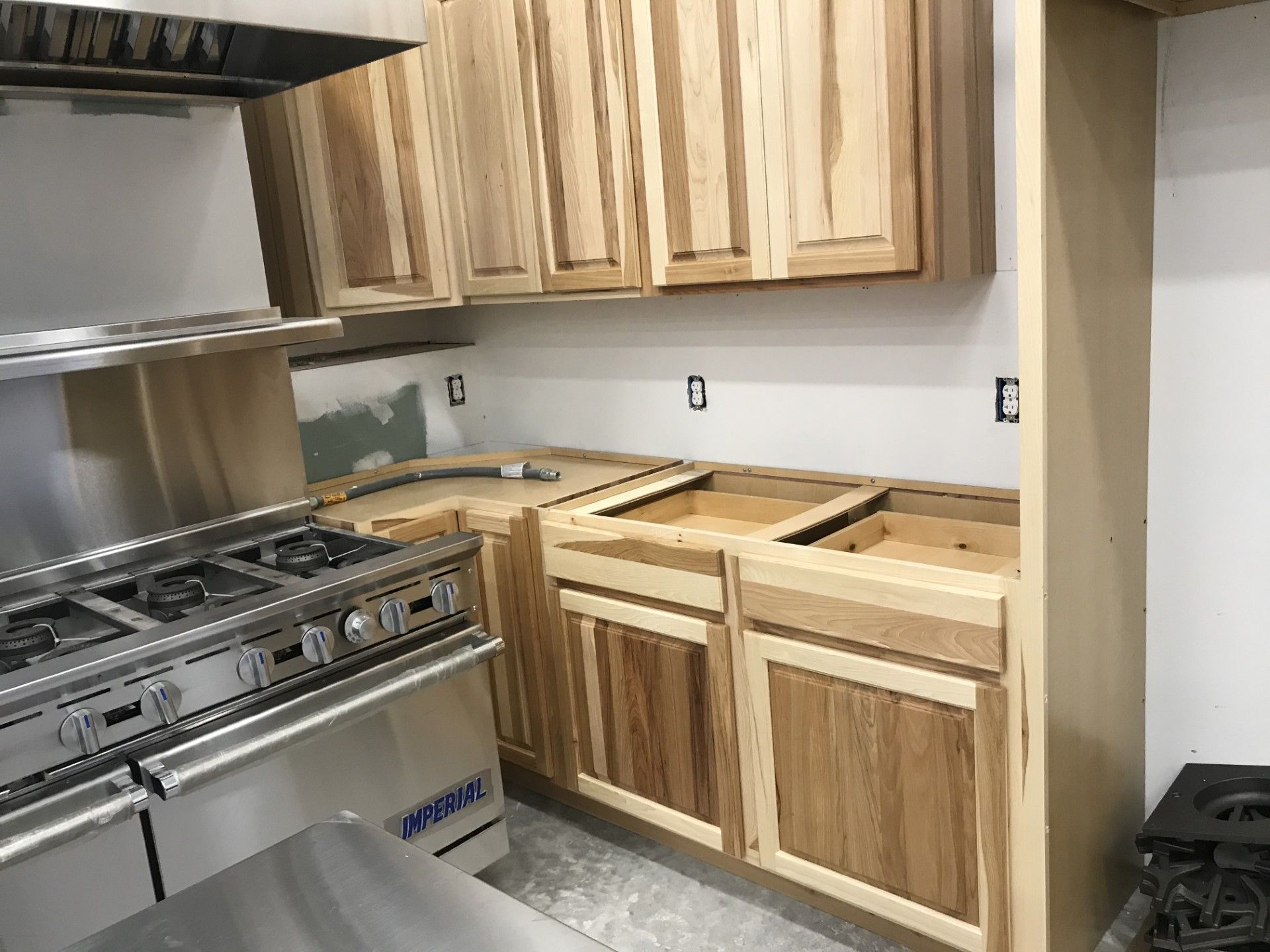 A kitchen renovation in progress featuring newly installed light-wood upper and lower cabinets next to a stainless range.