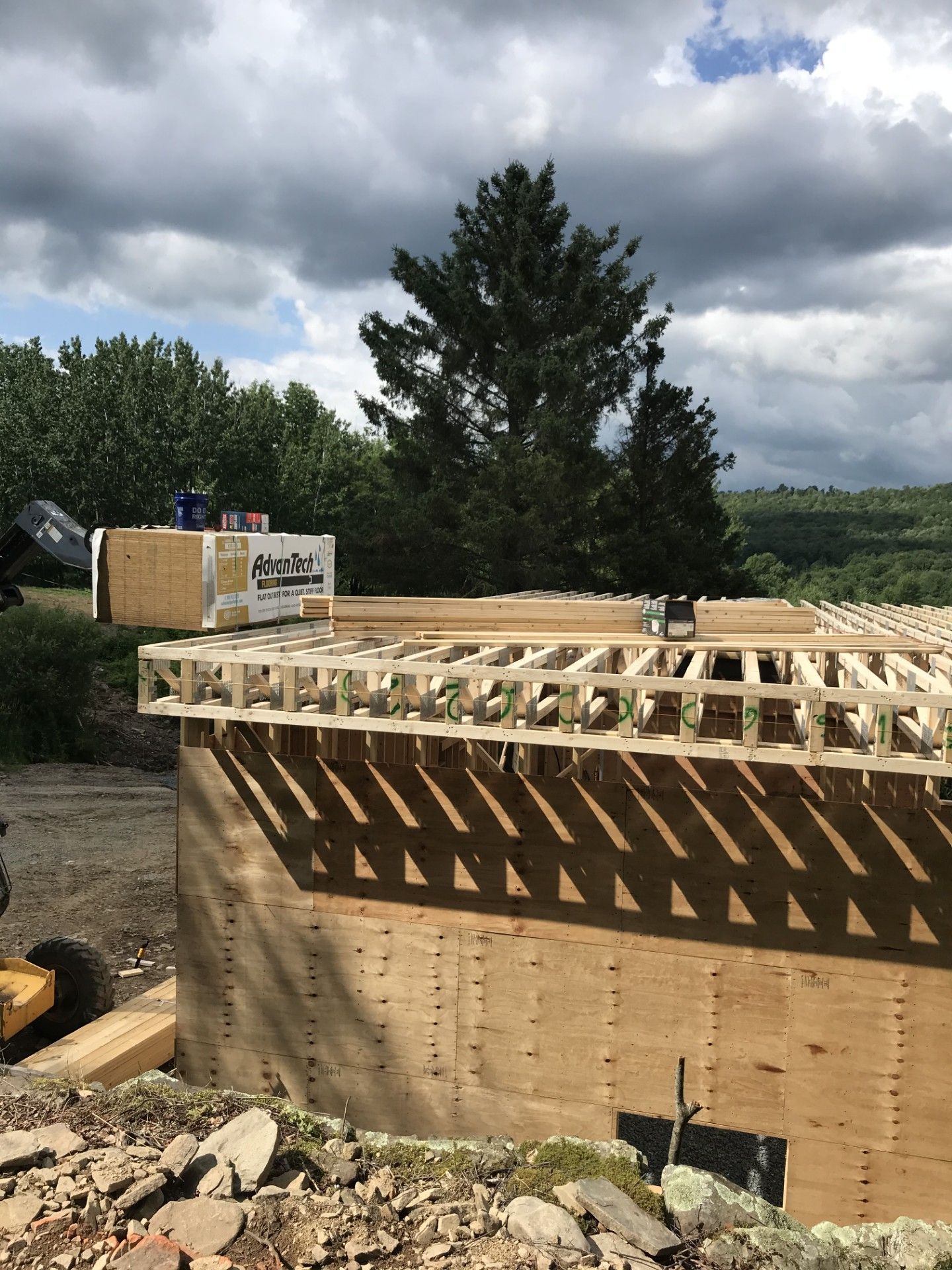 Construction site featuring a plywood-sheathed foundation wall topped with a wood floor joist system under a cloudy sky.