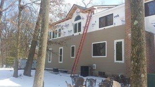 House with tan siding under construction, ladder against the side, snow on the ground.
