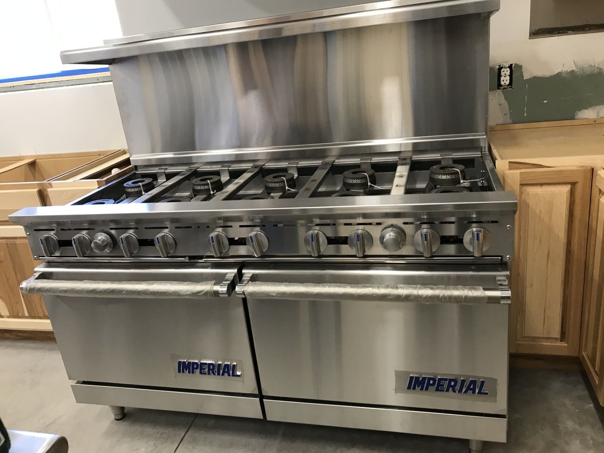 A stainless steel Imperial brand 10-burner commercial gas range standing in a kitchen under construction.