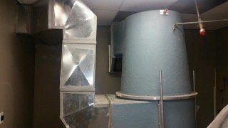 Metal HVAC ductwork on a wall, connected to a large, cylindrical ventilation system.