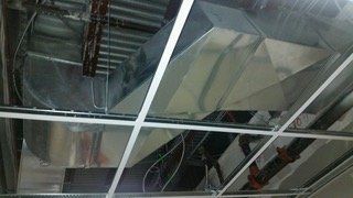 Metal HVAC ductwork installed above a suspended ceiling grid, in a construction setting.