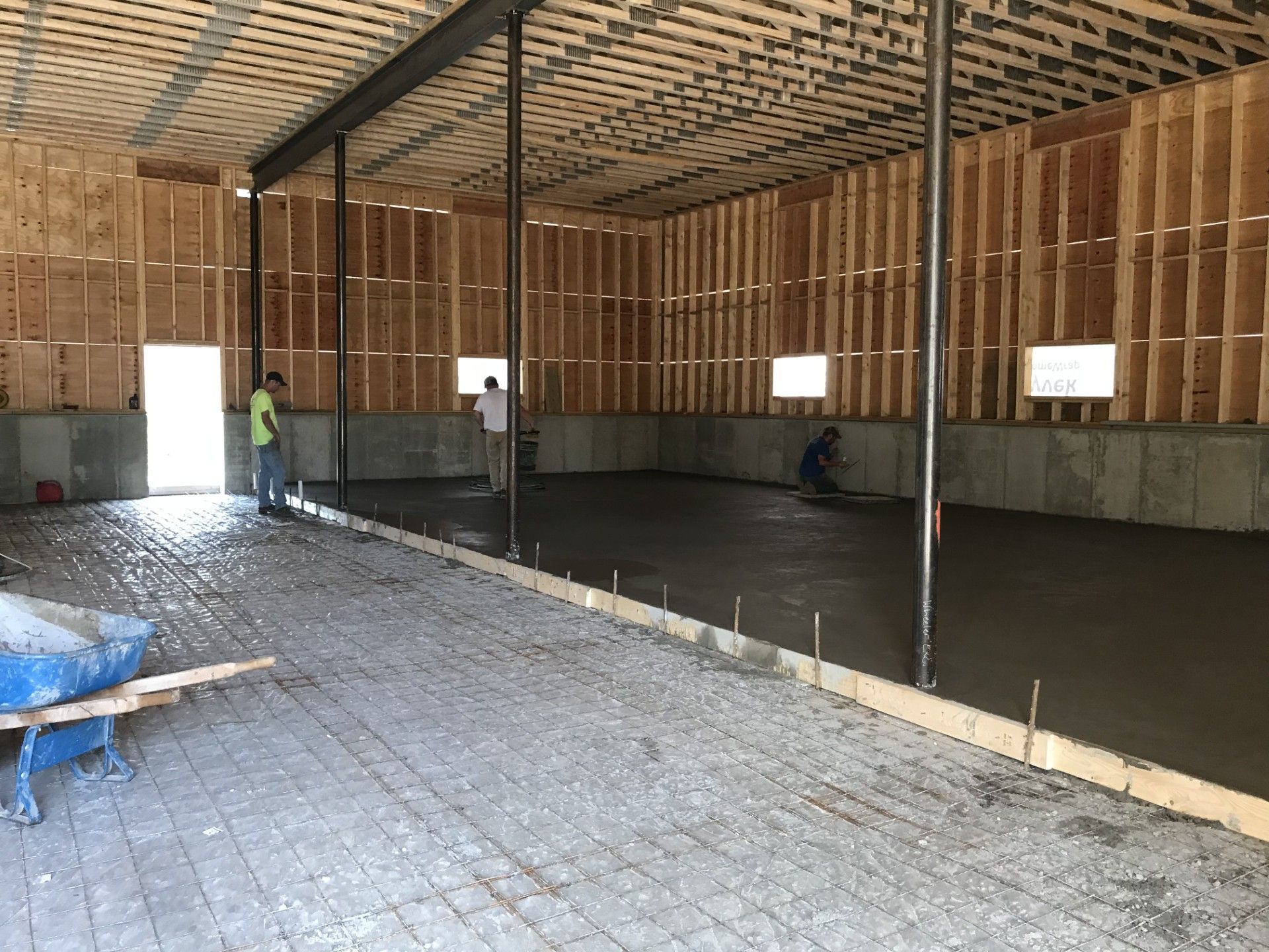Workers finish a newly poured concrete floor inside a framed building under construction.