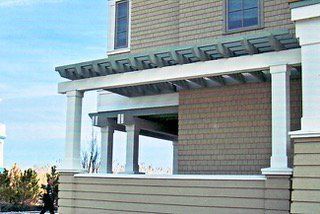 Exterior of a house with light green trim and a pergola over a porch.