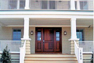 Beige house front with wooden double doors, porch, and white columns.